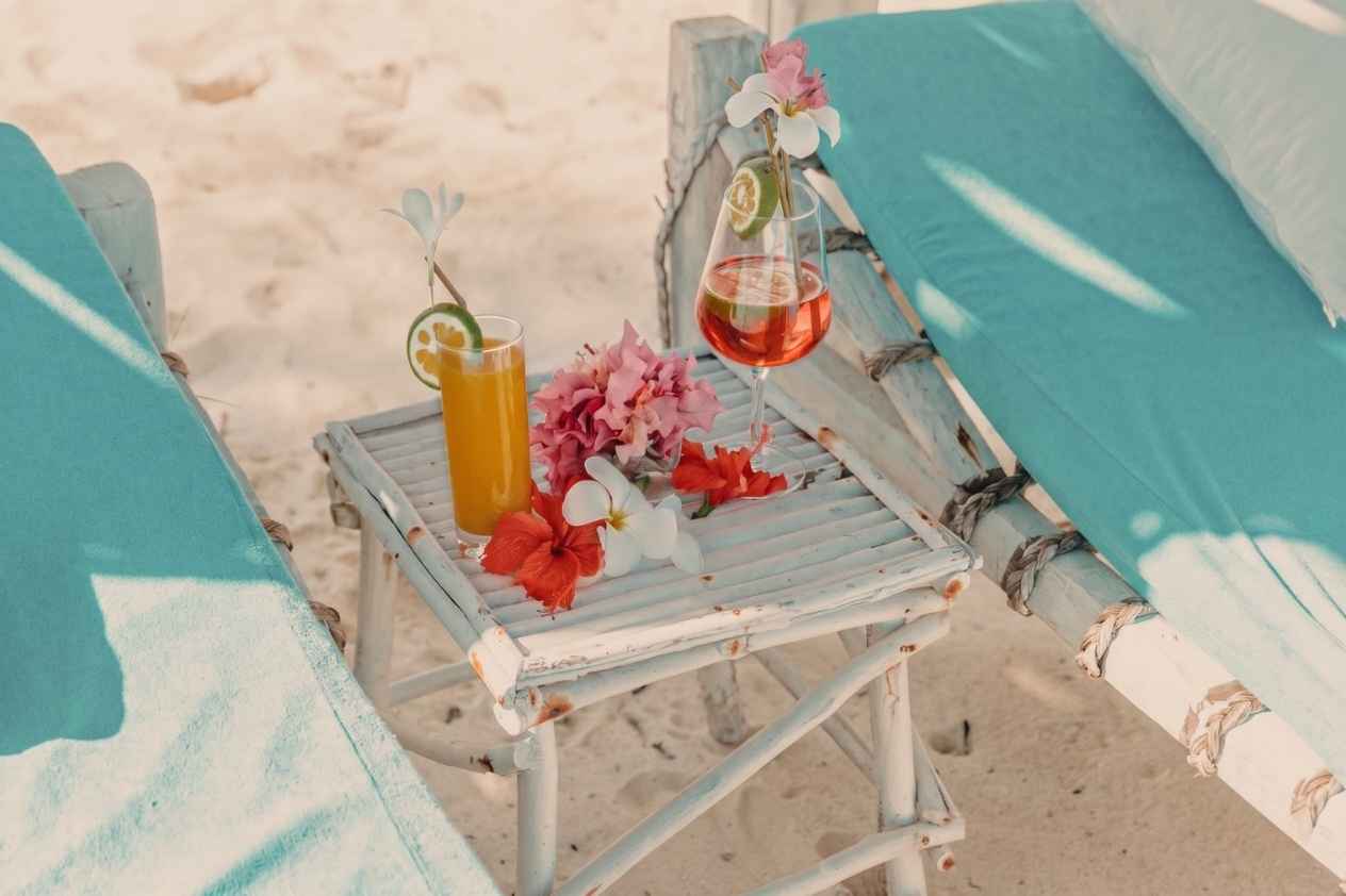 Two refreshing drinks garnished with tropical flowers on a weathered wooden table at Exploreans Malaika Beach Club, Kenya