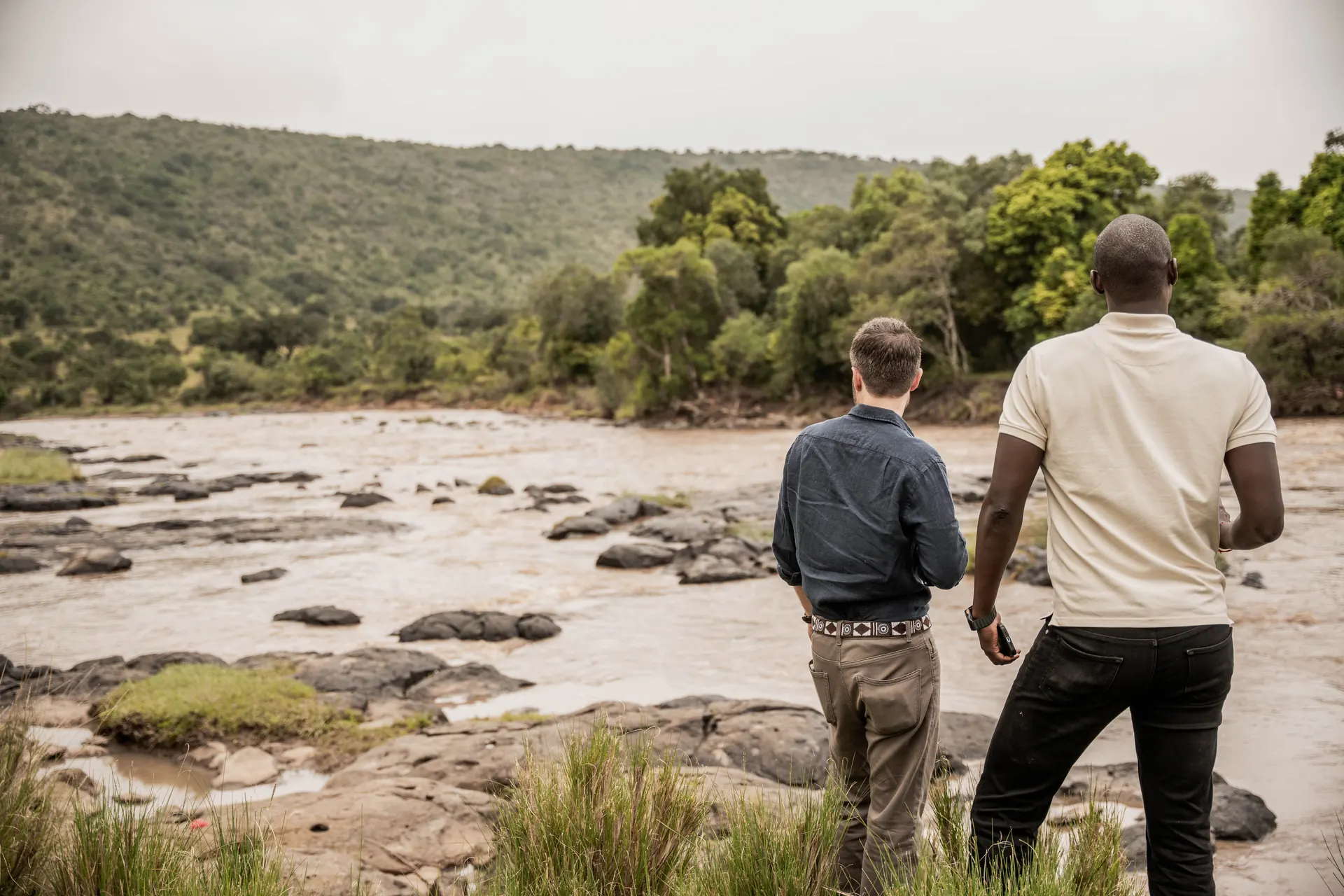 A guide and a guest standing among the rocks of the Mara River