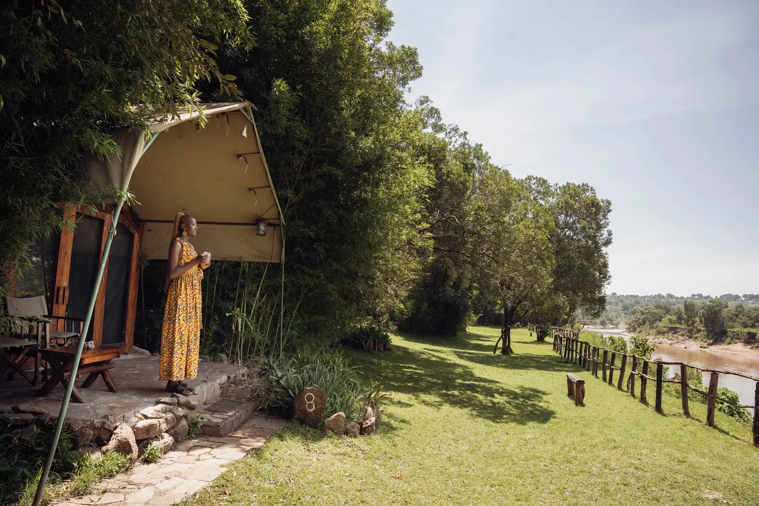 A guest on the terrace of a river tent, with the lawn running down to the Mara River