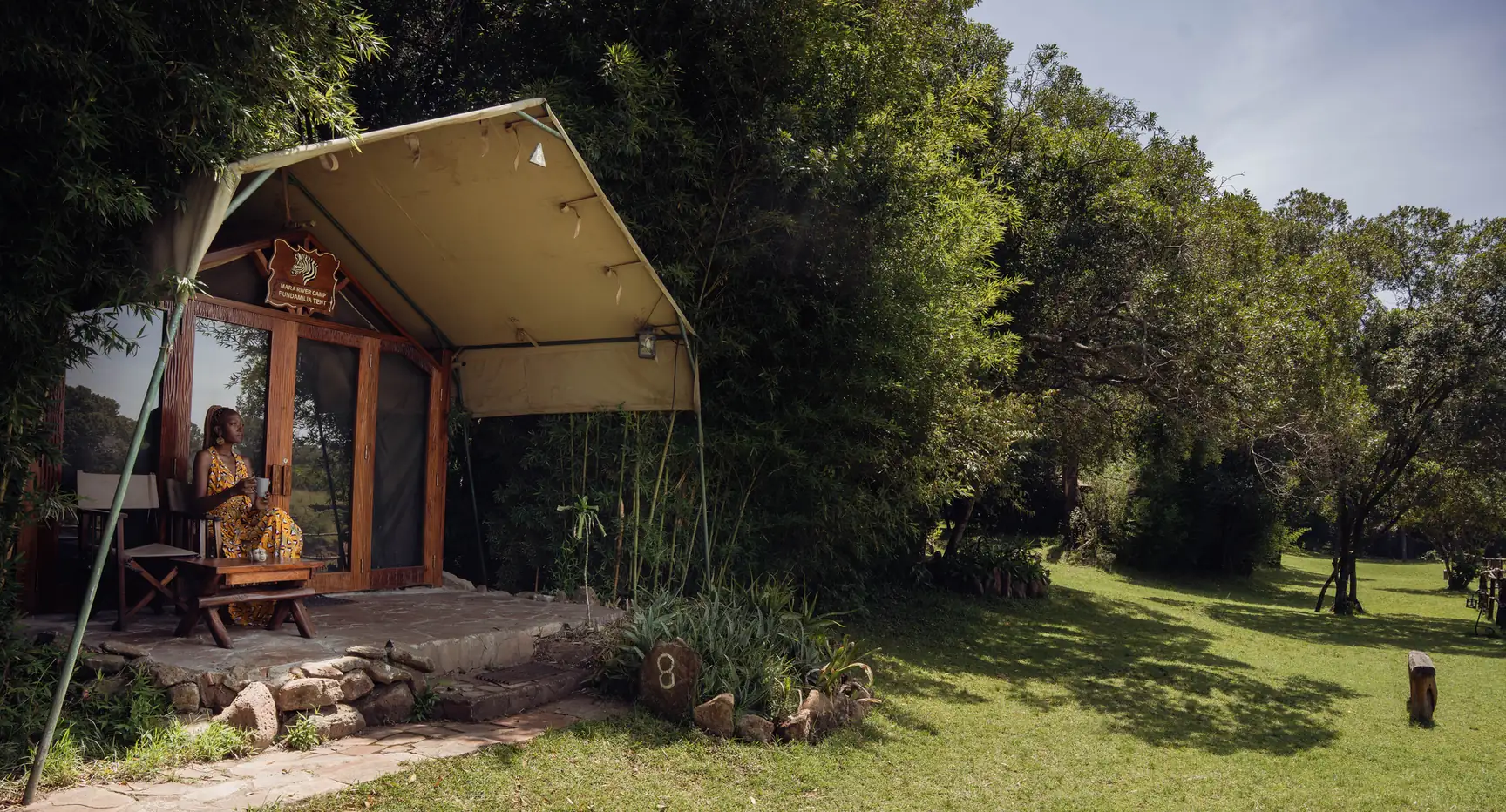 A guest with a cup of coffee on the terrace of a river tent above the Mara River