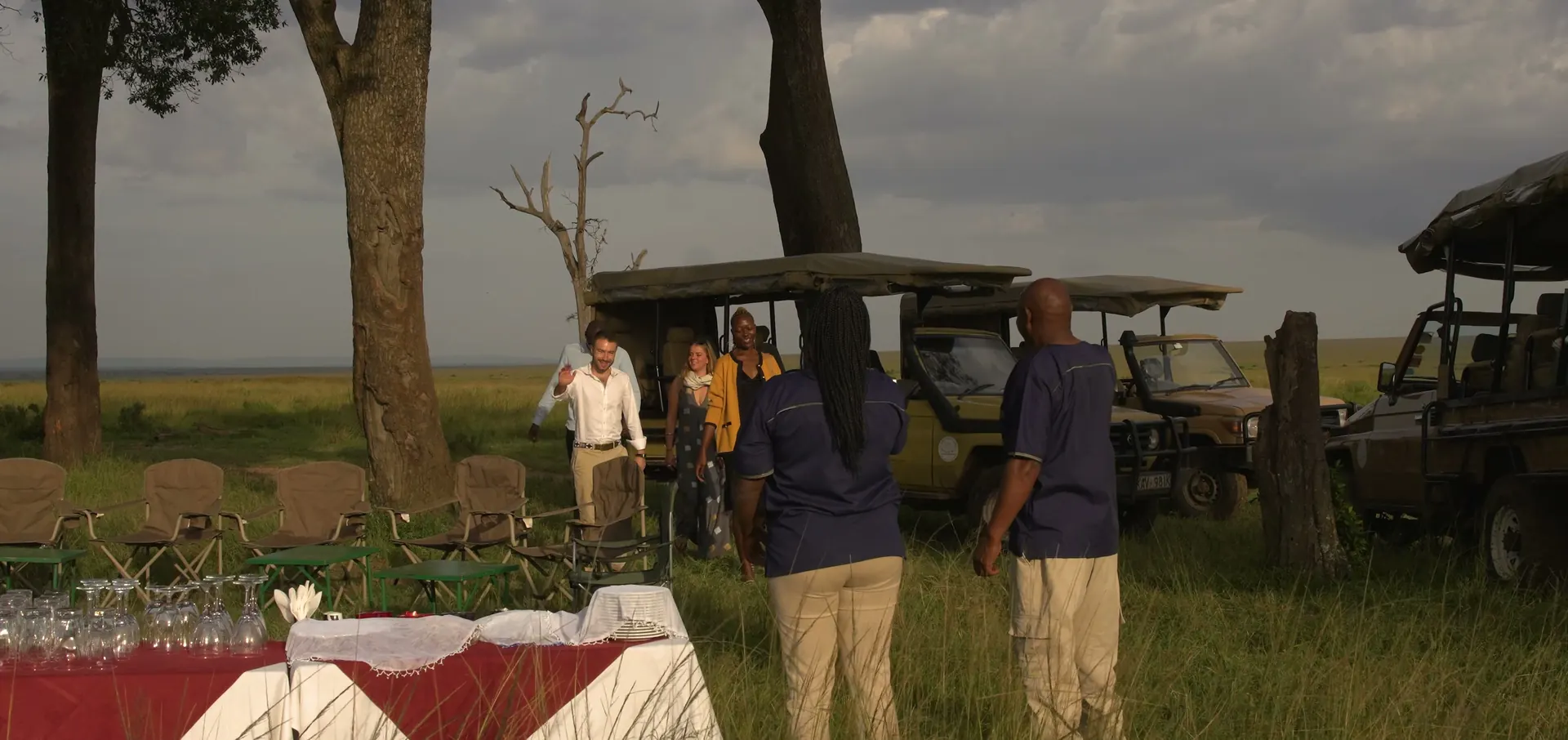 The camp team laying a table with a red cloth on the plains beside the safari vehicles