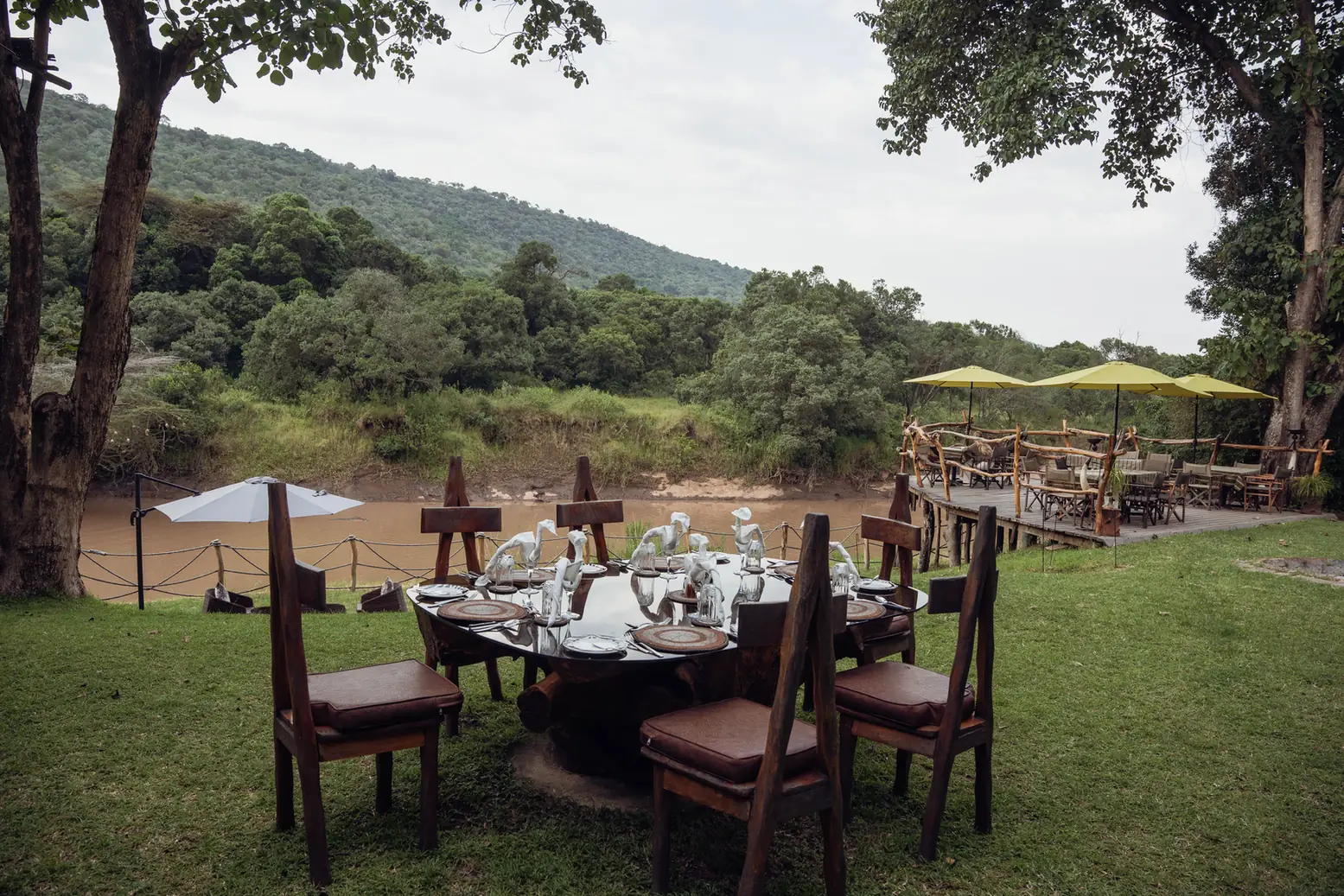 A table laid for lunch on the lawn above the river, with umbrellas on the deck behind