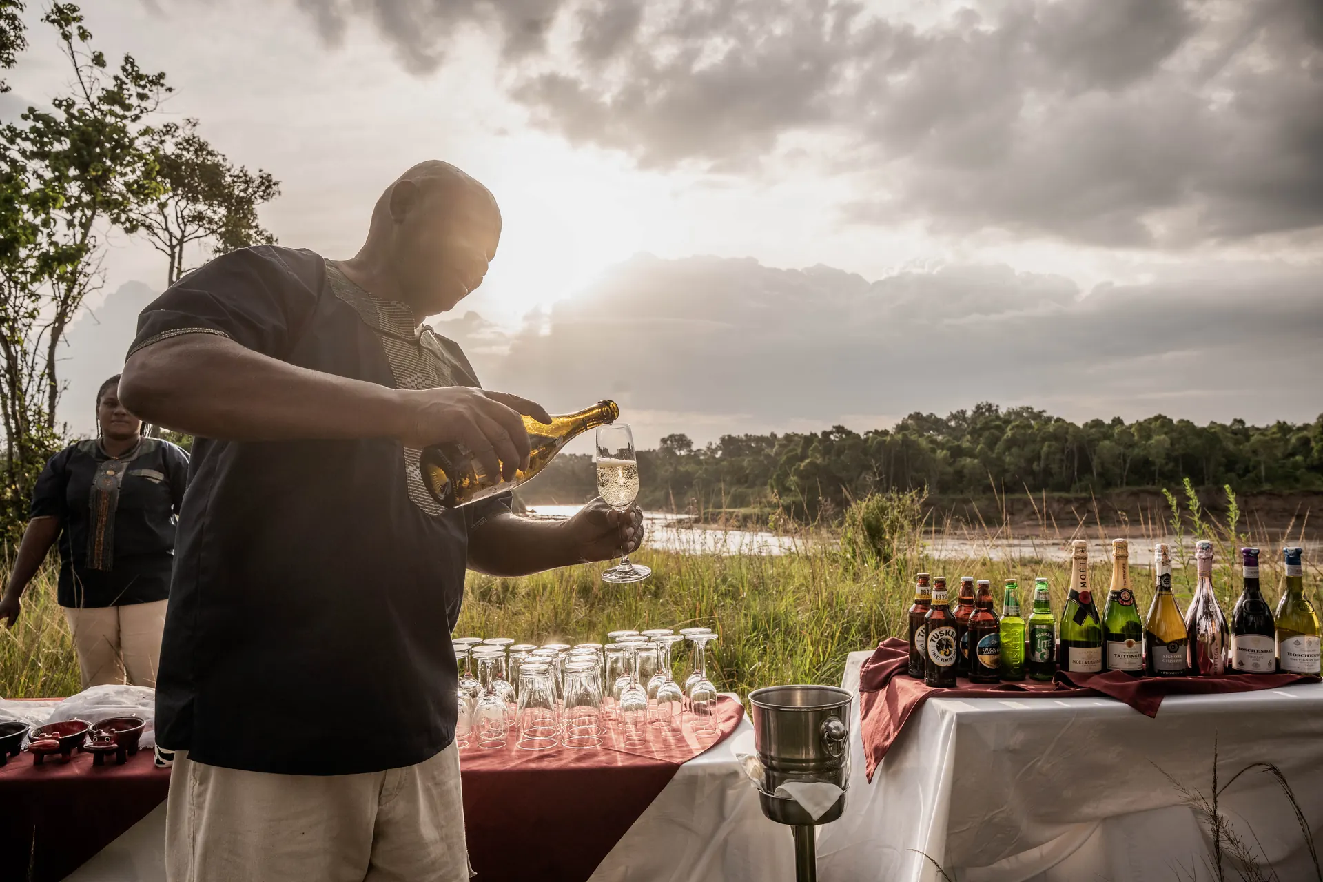 A guide pouring sparkling wine at a sundowner table on the plains