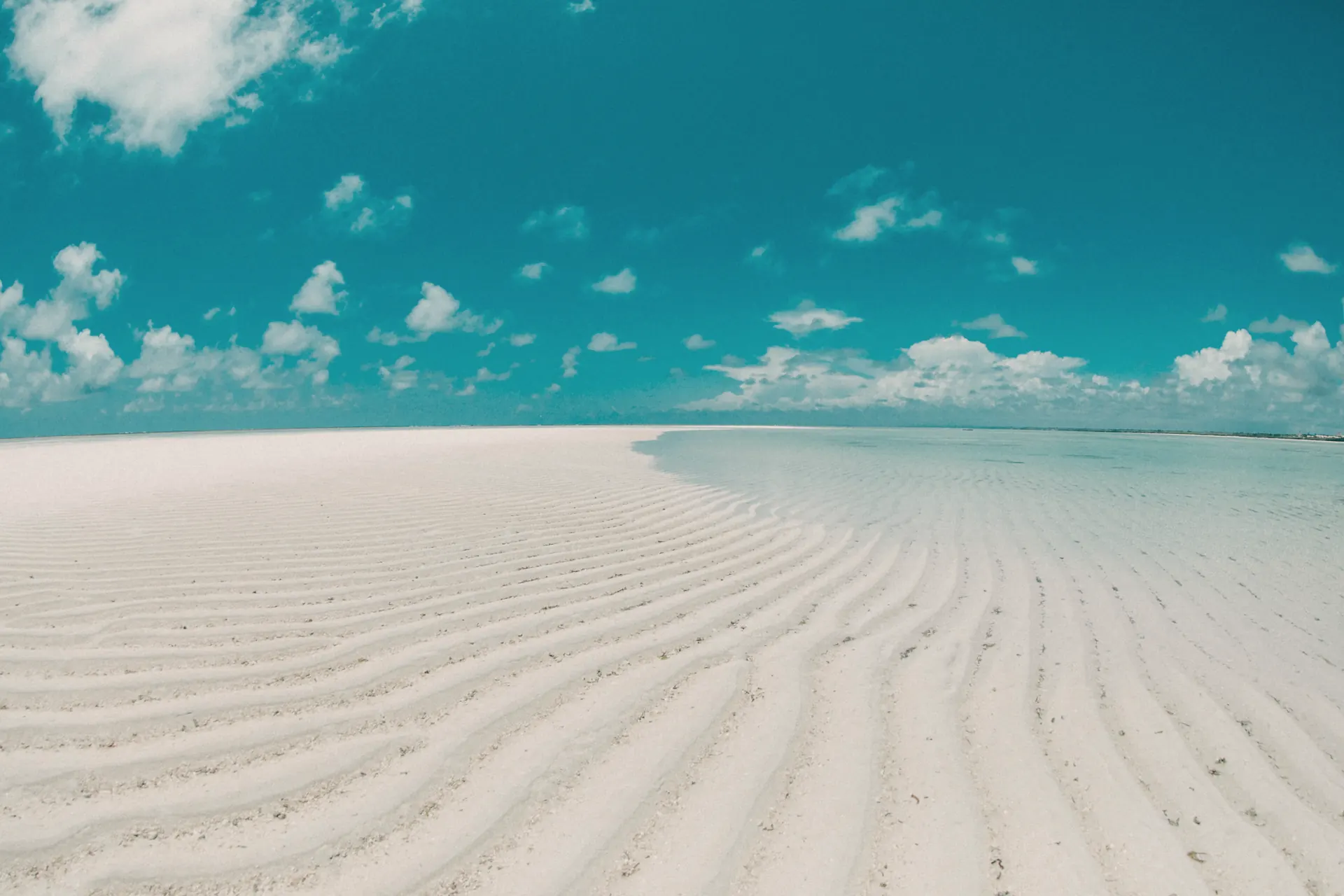 Rippled white sand and shallow turquoise water at low tide on Mayungu Bay