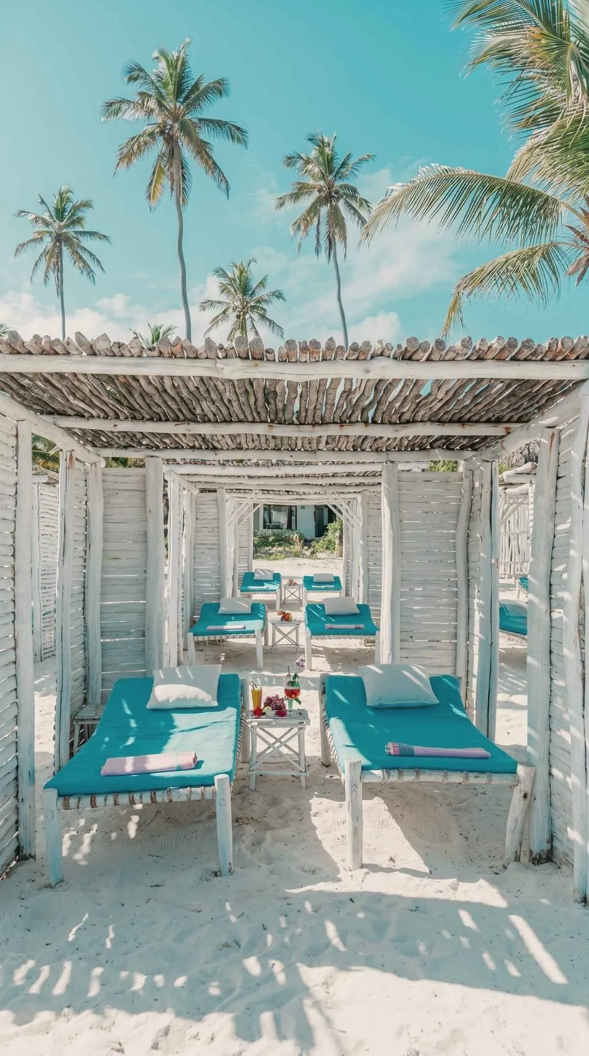 Whitewashed gazebos and turquoise sunbeds on the sand at the beach club