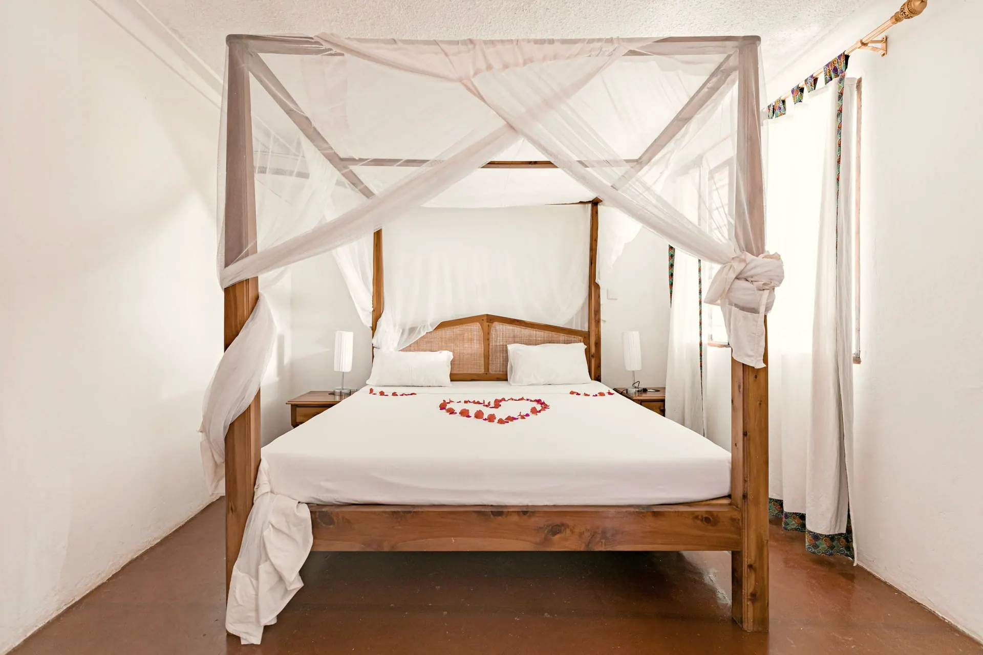 A villa bedroom with a four-poster bed and white linen